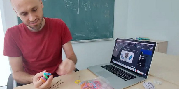 Jan Smrek holds colorful rubber bands while sitting at a table with a laptop.